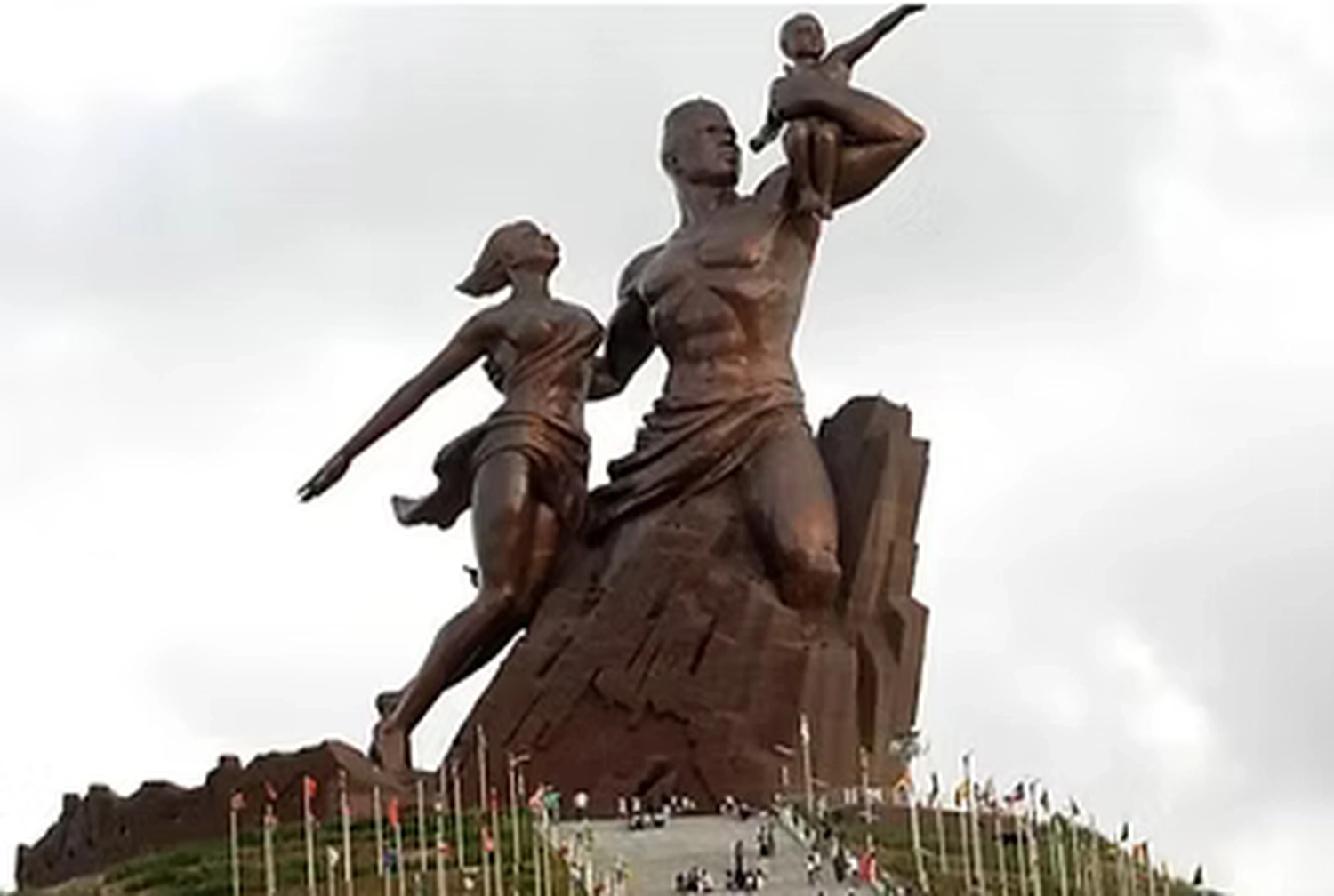 Gambia​ View Tours - Tourism services - A large bronze statue of a man, woman, and child standing on a hilltop, known as the African Renaissance Monument in Dakar, Senegal.