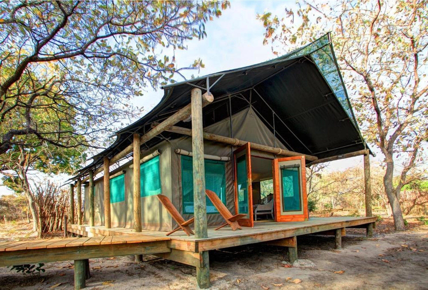 Gambia​ View Tours - Tourism services - A safari-style luxury tent elevated on a wooden deck in a wooded area, featuring a peaked canvas roof and wooden deck chairs.