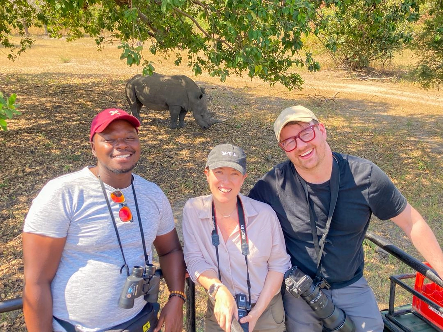 Gambia​ View Tours - Tourism services - Three tourists standing in Fathala wildlife Park with a rhinoceros behind.