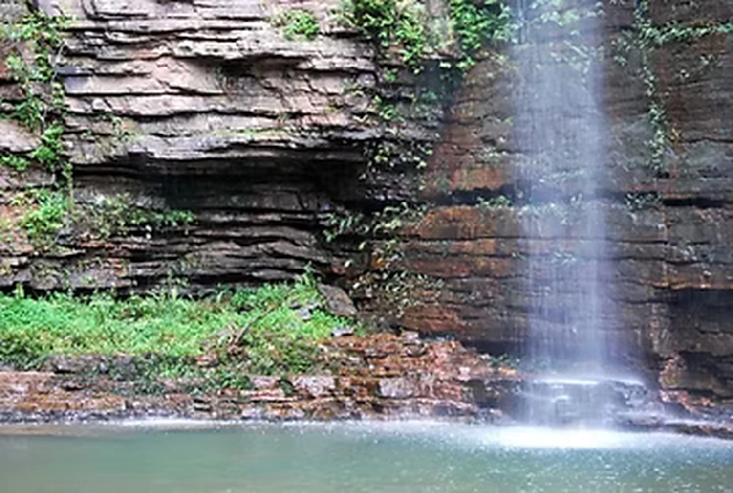 Gambia​ View Tours - Tourism services - A waterfall flowing over layered rock formations into a calm pool.